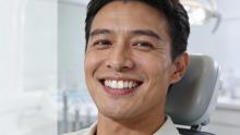 Smiling Indian male dentist with perfect white teeth, wearing white coat, close-up portrait in modern clinic for Gurgaon dental services.