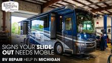 An RV parked inside a workshop garage undergoing a slide-out repair job